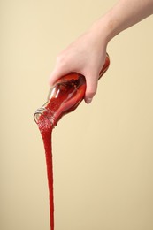 Photo of Woman pouring tasty ketchup from bottle on beige background, closeup