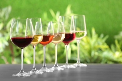 Row of glasses with different wines on grey table against blurred background. Space for text