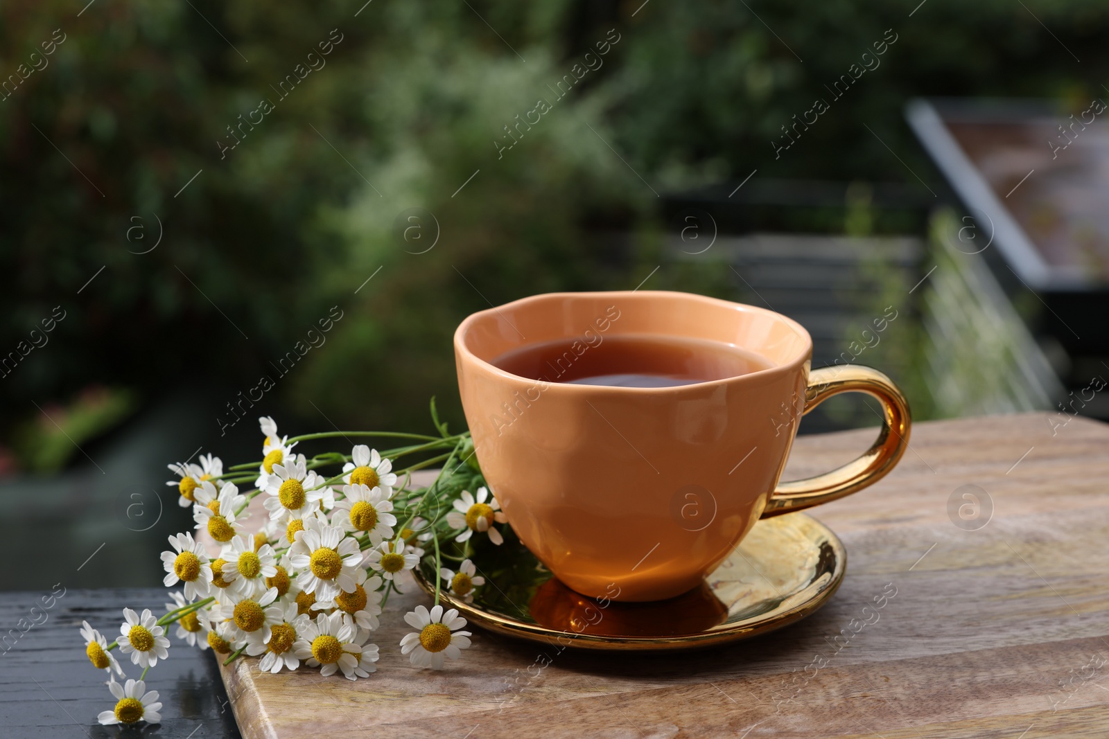 Photo of Cup of delicious chamomile tea and fresh flowers outdoors