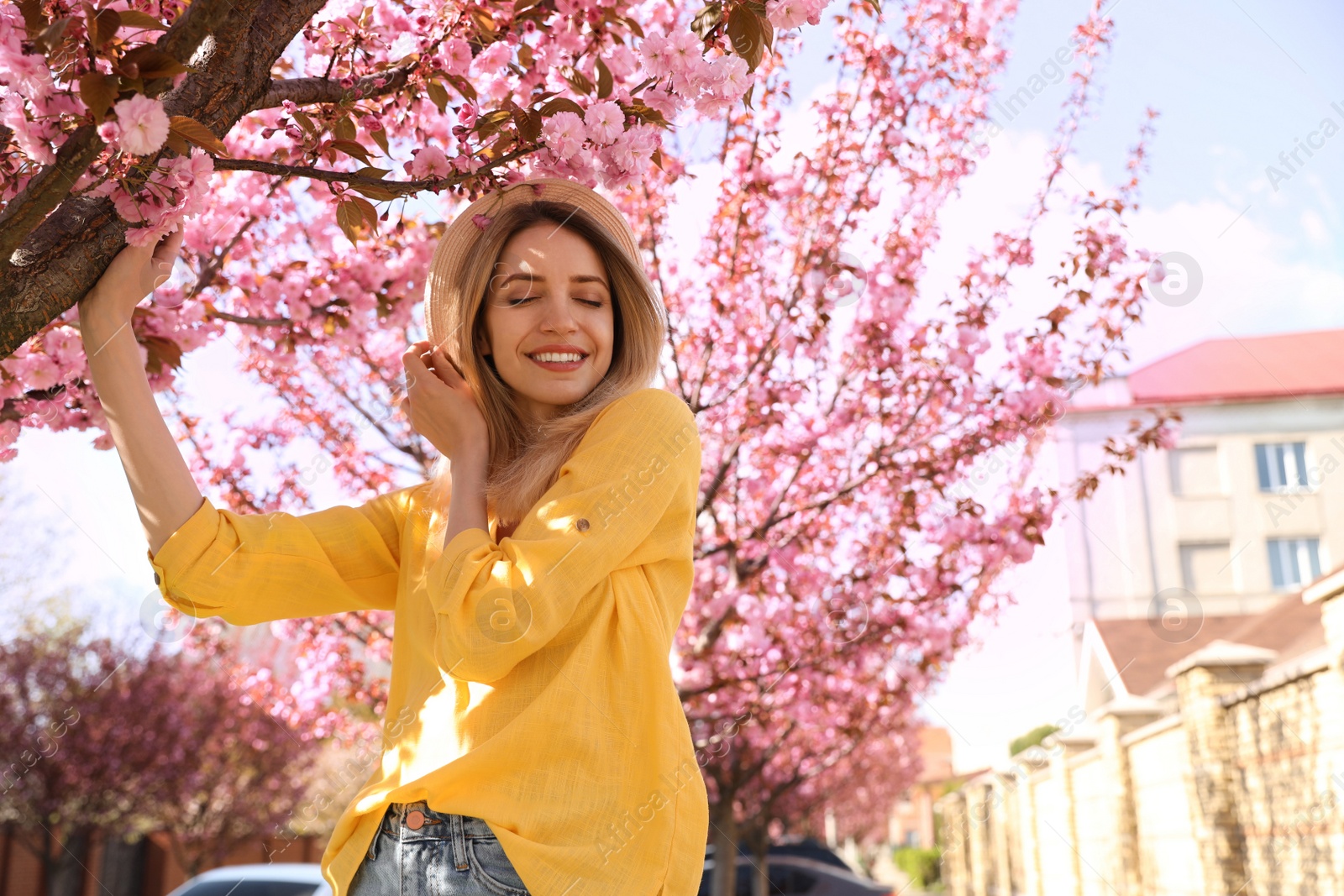 Photo of Happy stylish young woman near blossoming sakura tree outdoors. Spring look