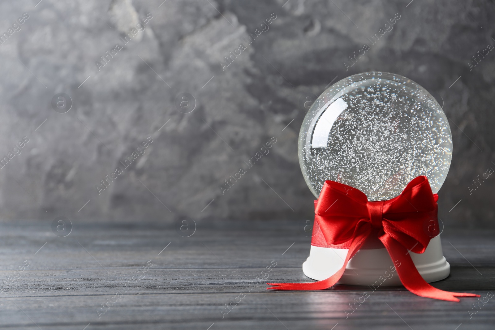 Photo of Beautiful Christmas snow globe with red bow on grey wooden table, space for text