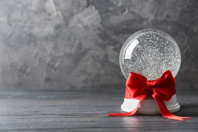 Photo of Beautiful Christmas snow globe with red bow on grey wooden table, space for text