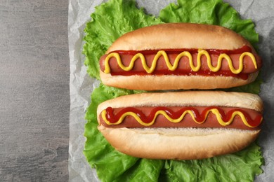 Photo of Delicious hot dogs with mustard, ketchup and lettuce on grey table, top view. Space for text