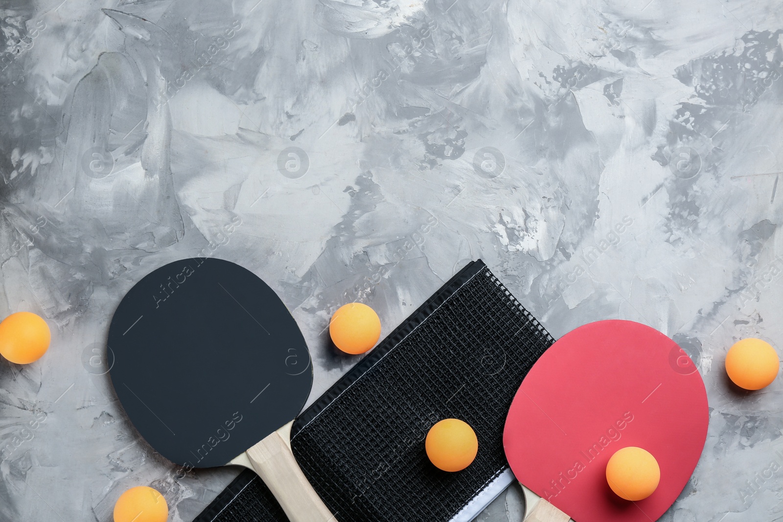 Photo of Ping pong rackets, net and balls on grey table, flat lay. space for text