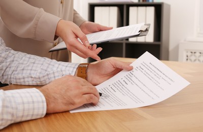 Businesspeople signing contract at wooden table indoors, closeup of hands