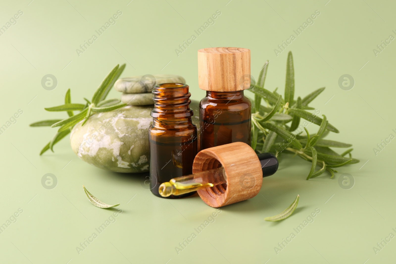 Photo of Aromatic essential oils in bottles, rosemary, pipette and pebble stones on green background