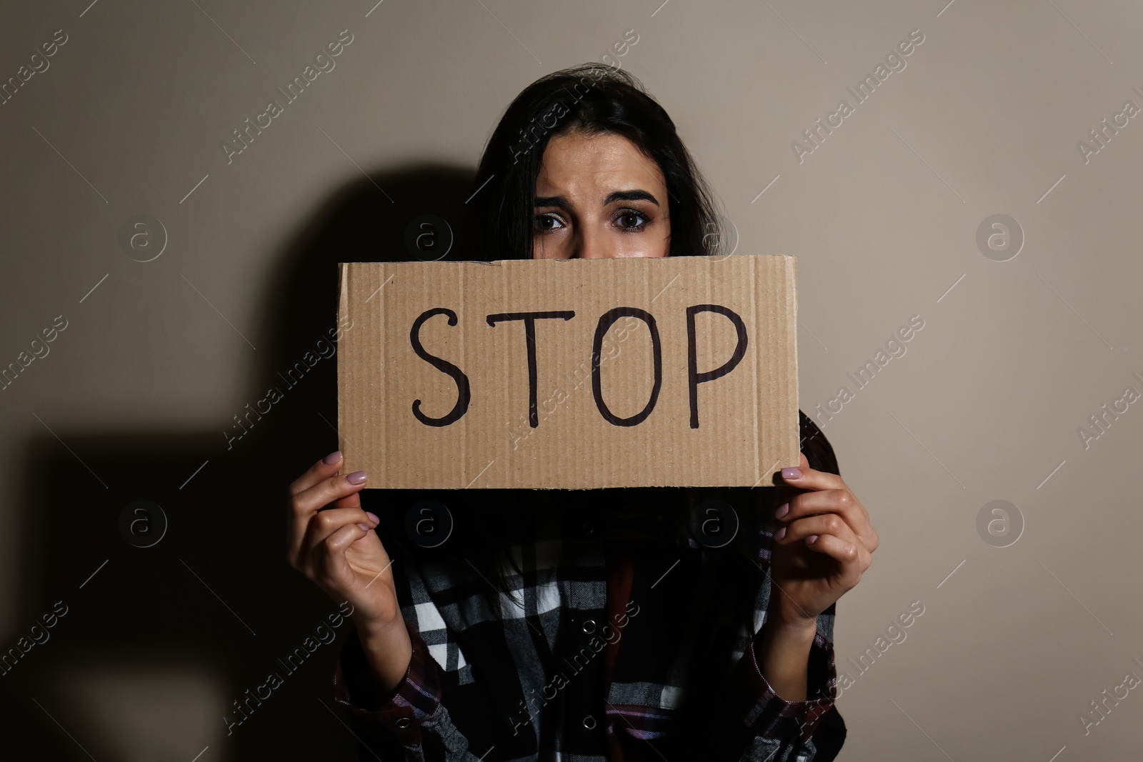 Photo of Abused young woman with sign STOP near beige wall. Domestic violence concept