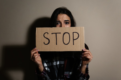 Abused young woman with sign STOP near beige wall. Domestic violence concept