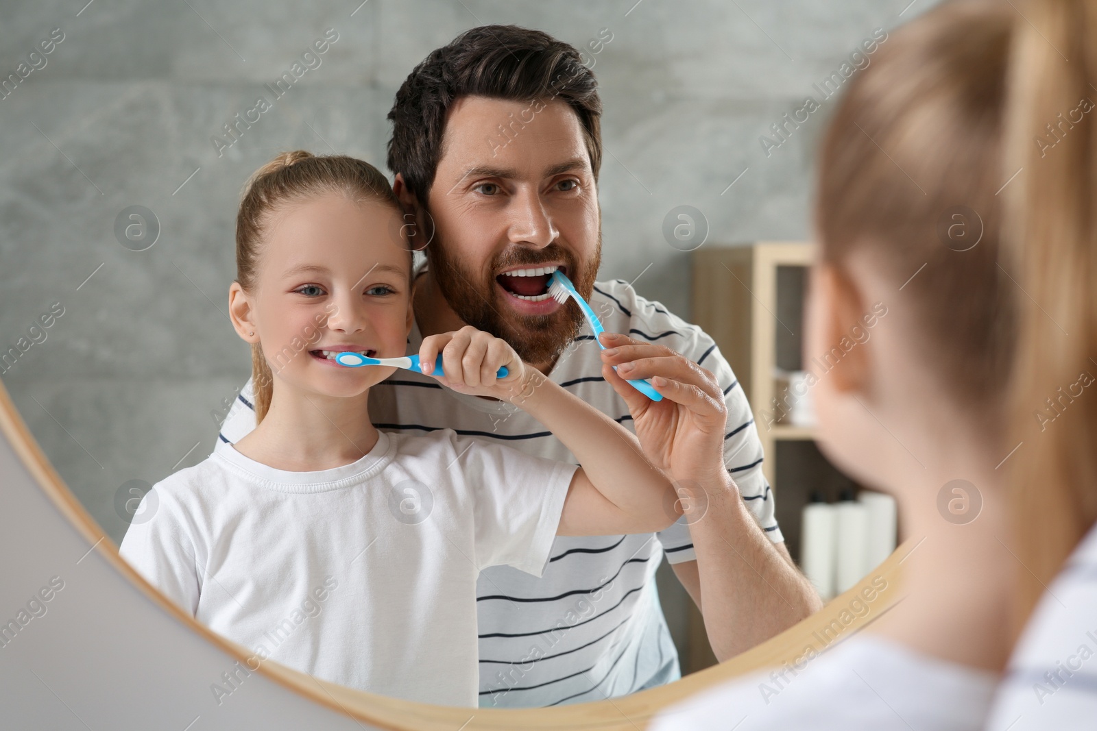 Photo of Father and his daughter brushing teeth together near mirror in bathroom