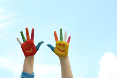 Photo of Kid with smiling faces drawn on palms against blue sky, closeup. Space for text