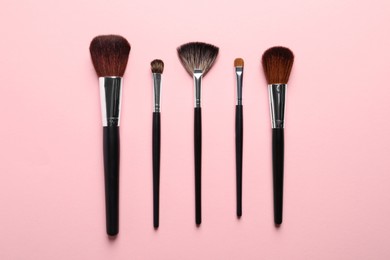 Photo of Different makeup brushes on pink background, flat lay