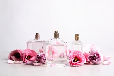 Photo of Bottles of perfume and beautiful flowers on light table