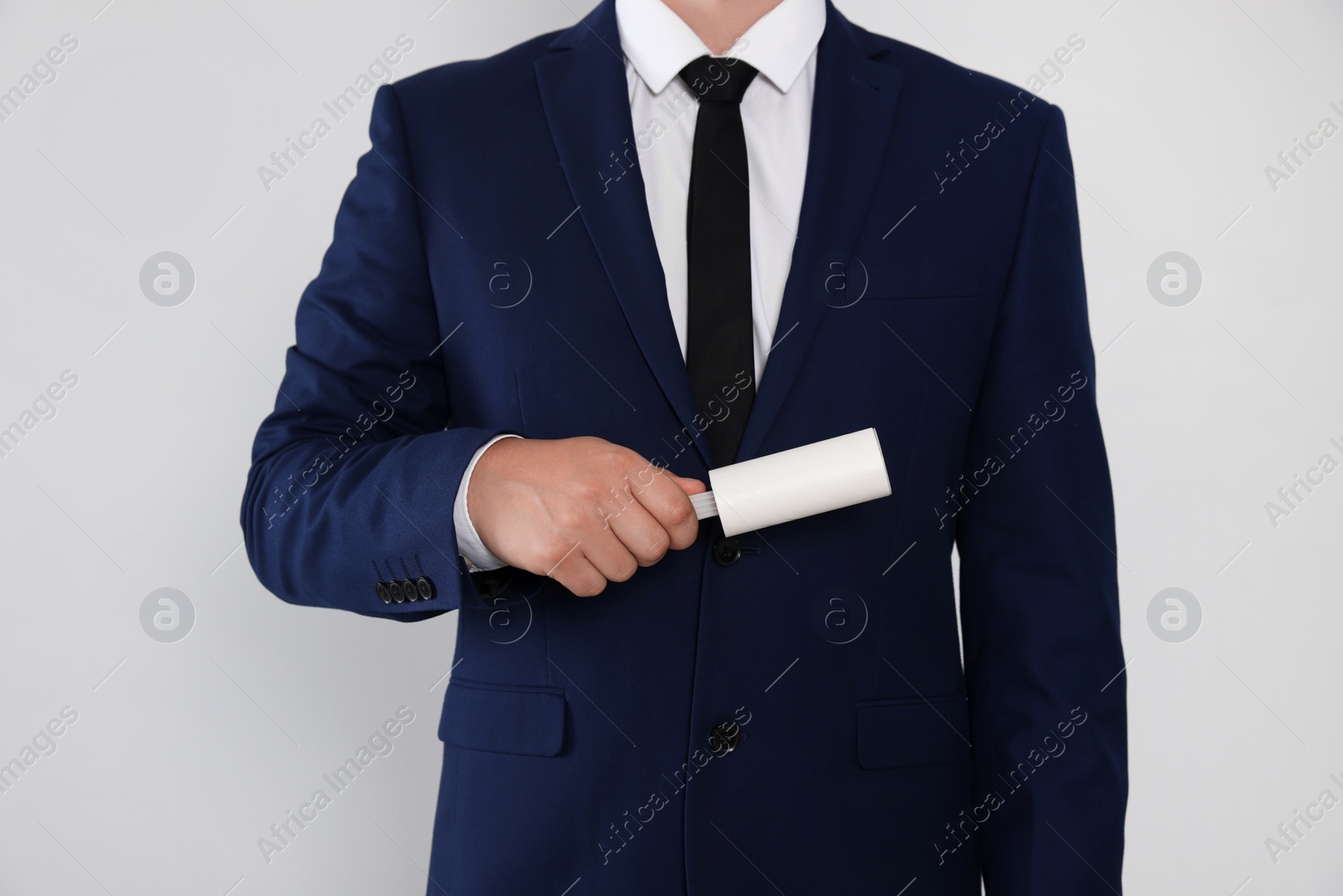 Photo of Man cleaning suit with lint roller on light grey background, closeup