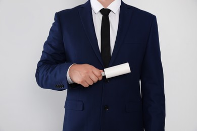 Man cleaning suit with lint roller on light grey background, closeup