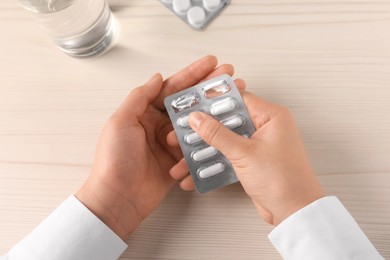 Woman with blister of pills at white wooden table, closeup