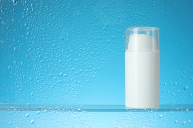 Photo of Bottle with moisturizing cream on light blue background, view through wet glass. Space for text