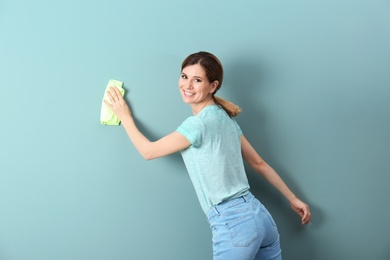 Photo of Young woman cleaning color wall with rag