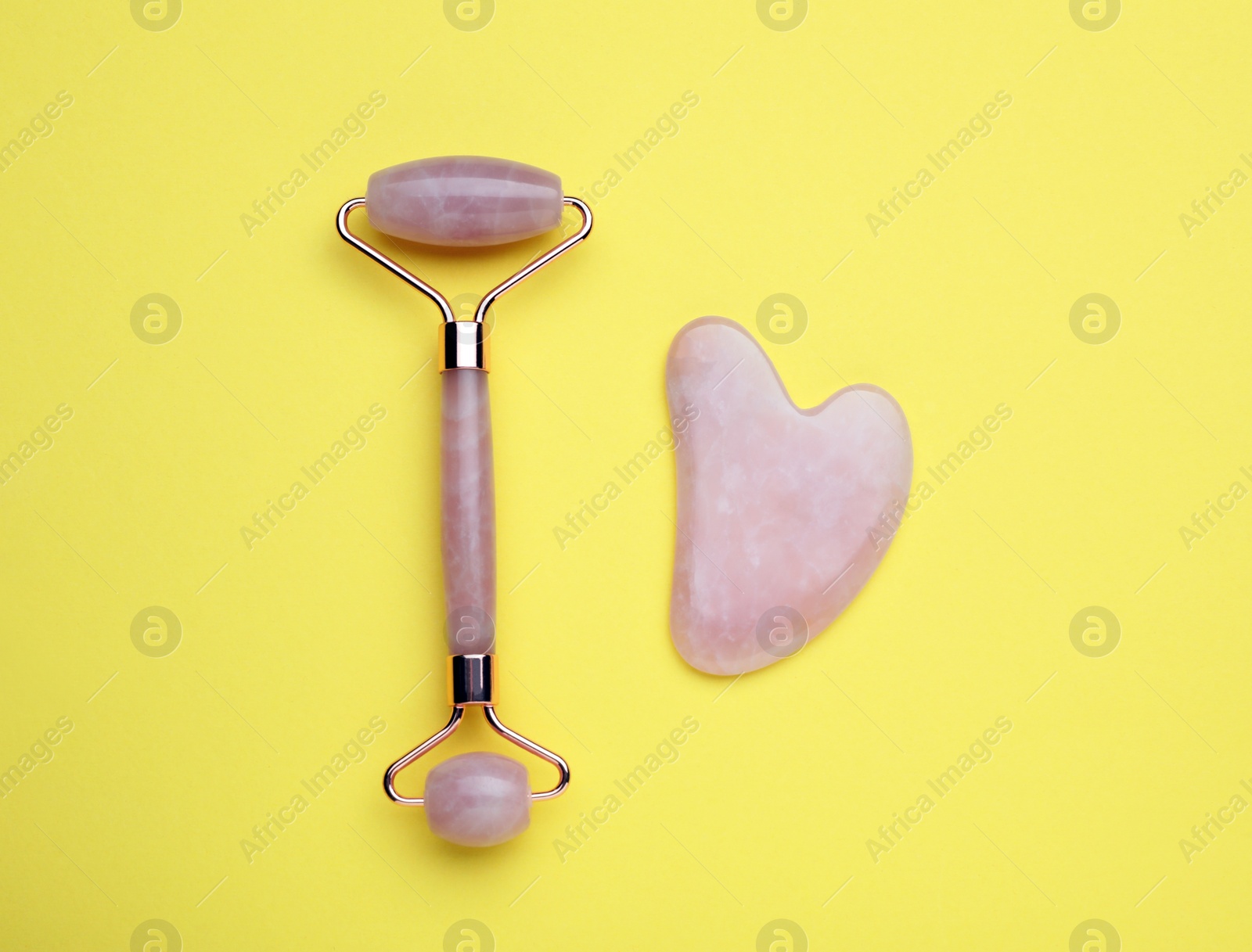 Photo of Gua sha stone and face roller on yellow background, flat lay