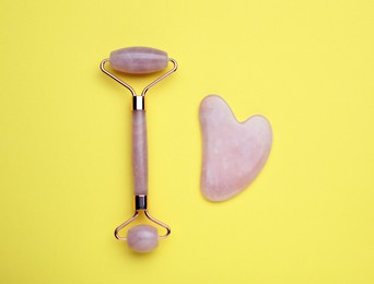 Gua sha stone and face roller on yellow background, flat lay