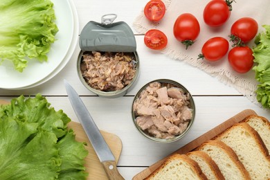 Photo of Tin cans with canned tuna and products on white wooden table, fat lay