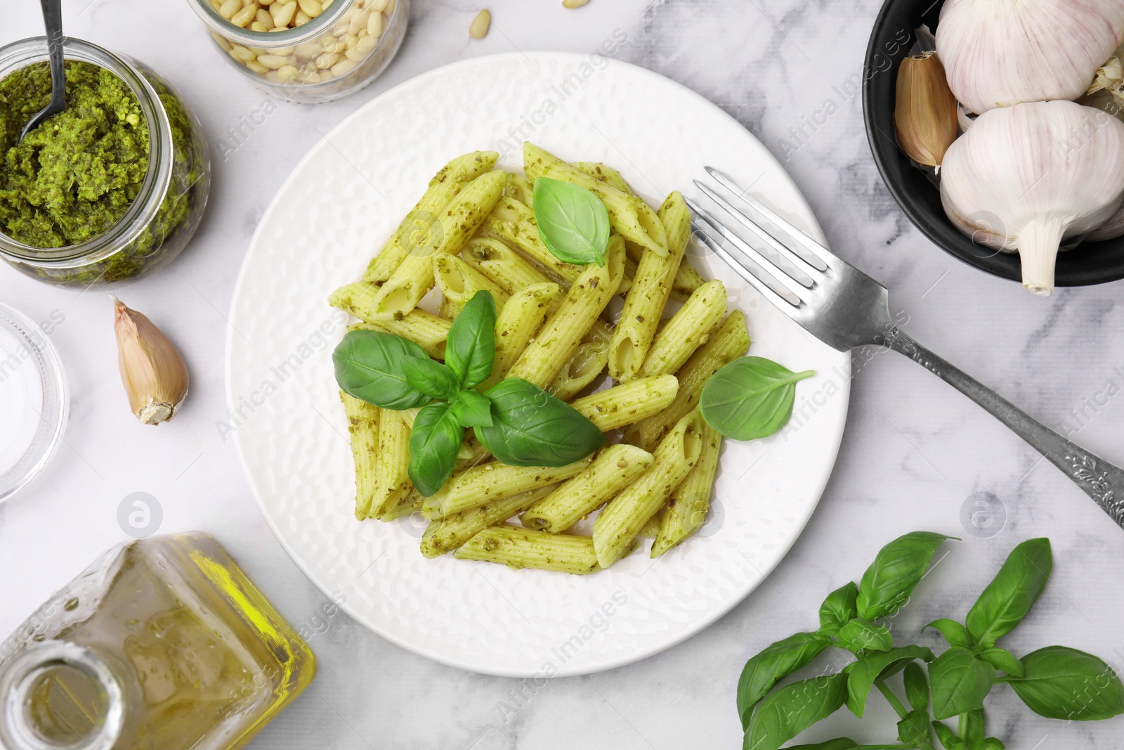 Photo of Delicious pasta with pesto sauce and ingredients on white marble table, flat lay