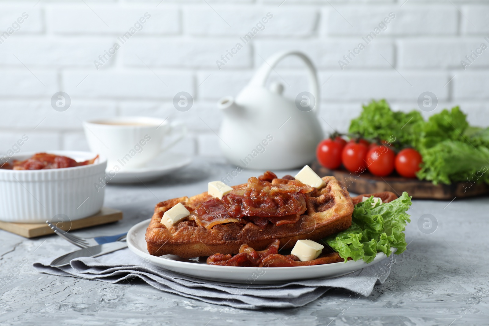 Photo of Delicious Belgium waffles served with fried bacon and butter on grey table, space for text