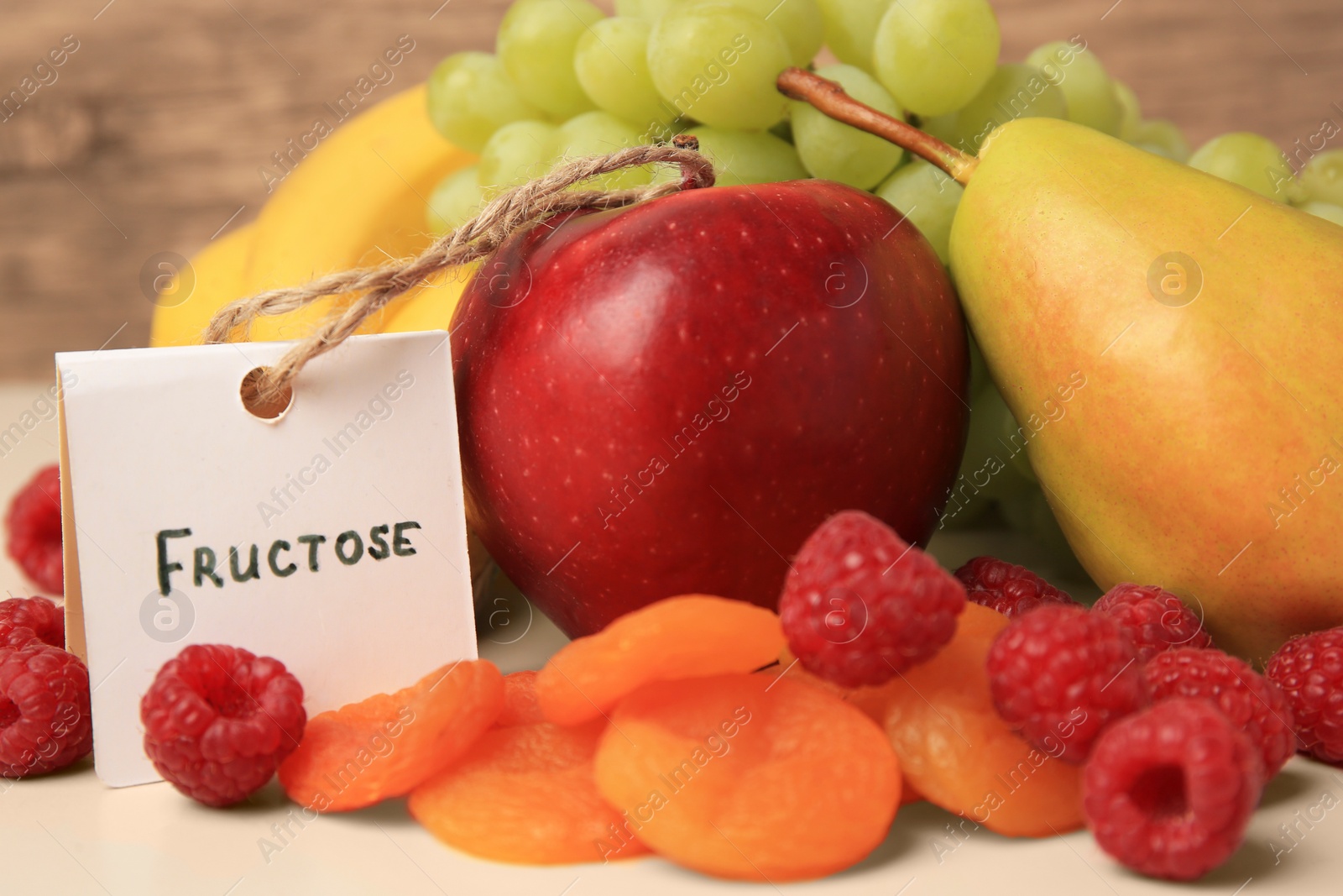 Photo of Card with word Fructose, delicious ripe fruits, raspberries and dried apricots on table, closeup