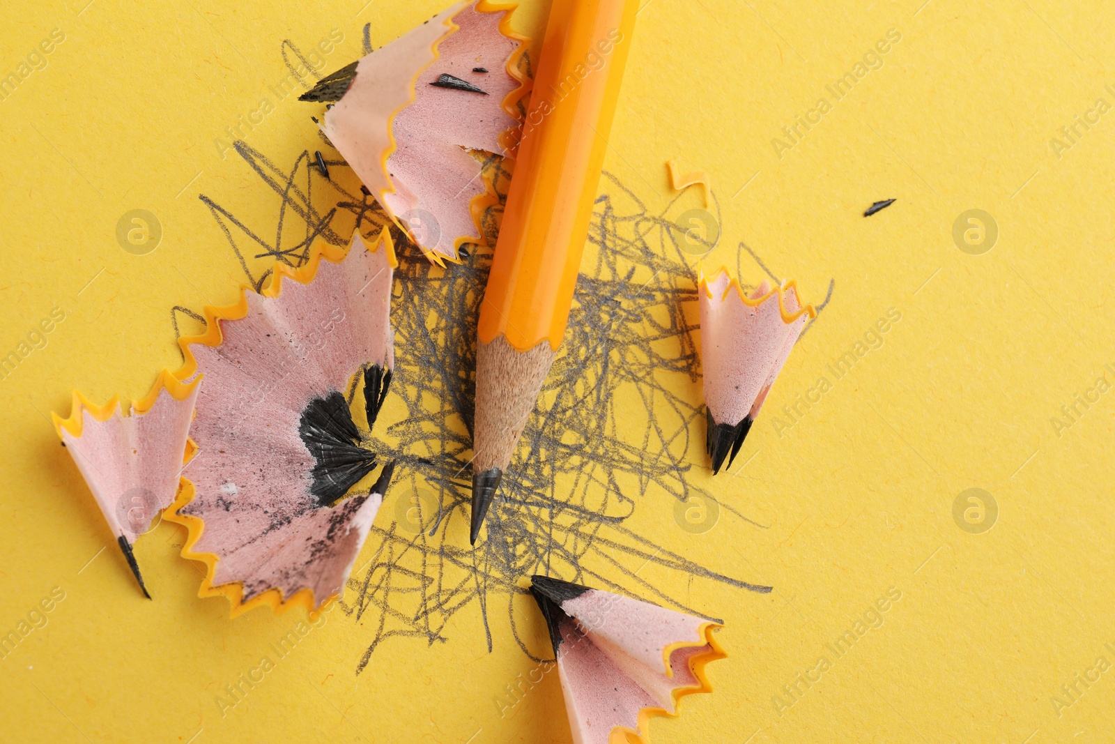 Photo of One sharp graphite pencil, scribbles and shavings on yellow background, top view