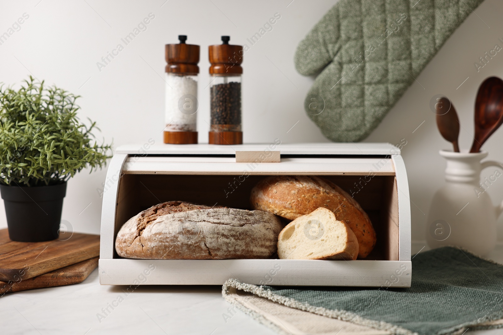 Photo of Wooden bread basket with freshly baked loaves on white marble table in kitchen