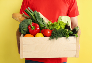 Photo of Courier with fresh products on yellow background, closeup. Food delivery service