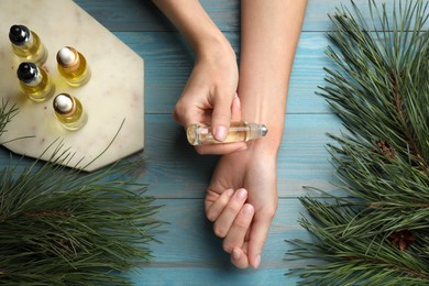 Photo of Woman applying pine essential oil on wrist at light blue wooden table, top view