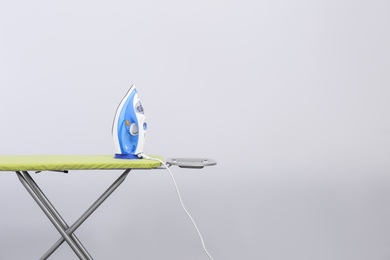 Photo of Modern electric iron on board against light background, space for text