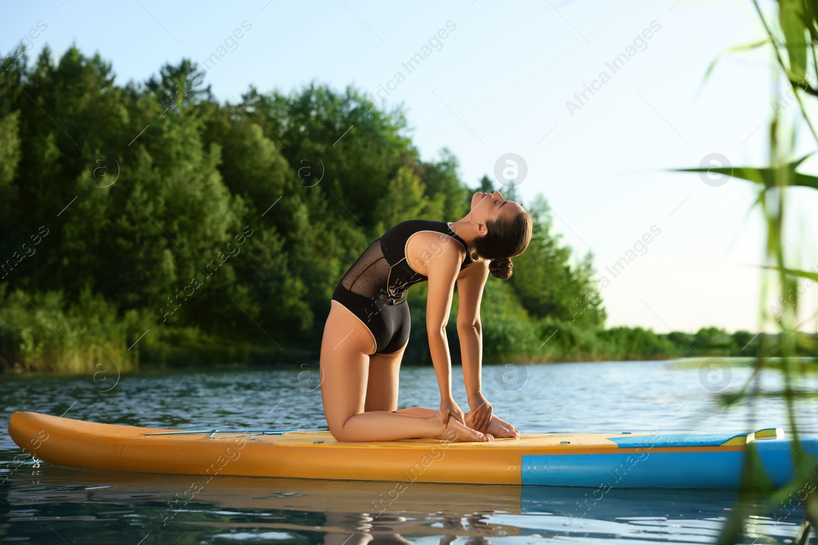 Photo of Young woman practicing yoga on color SUP board on river