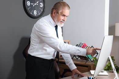 Senior boss having online meeting on computer at wooden table in modern office