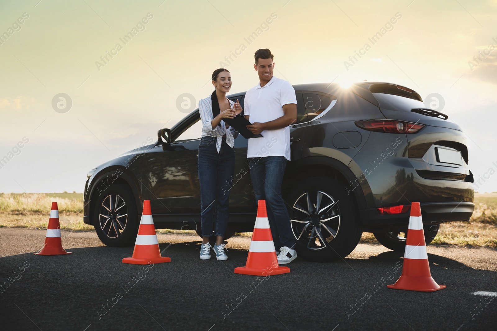 Photo of Instructor with clipboard near car and his student outdoors. Driving school exam