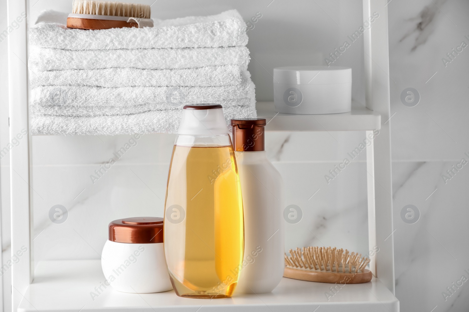 Photo of Stack of towels, brushes, shampoo and other toiletries on shelves near white marble wall