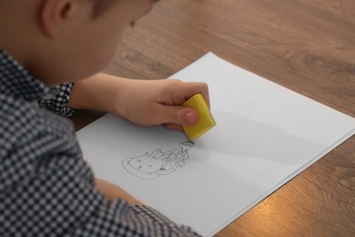 Little boy erasing mistake in his notebook at wooden desk, closeup