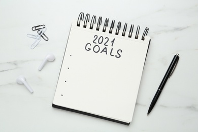 Photo of Notebook with inscription 2021 Goals, new year aims. Objects on white marble table, flat lay