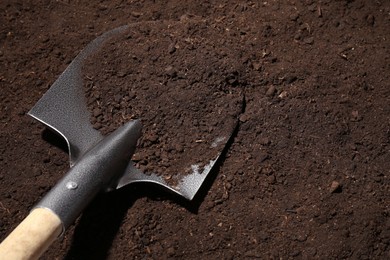 Photo of Metal shovel on fertile soil, space for text. Gardening tool