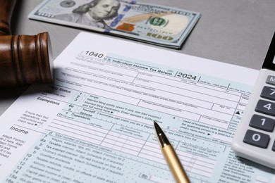Photo of Tax return form, gavel, dollar banknote and calculator on grey table, closeup