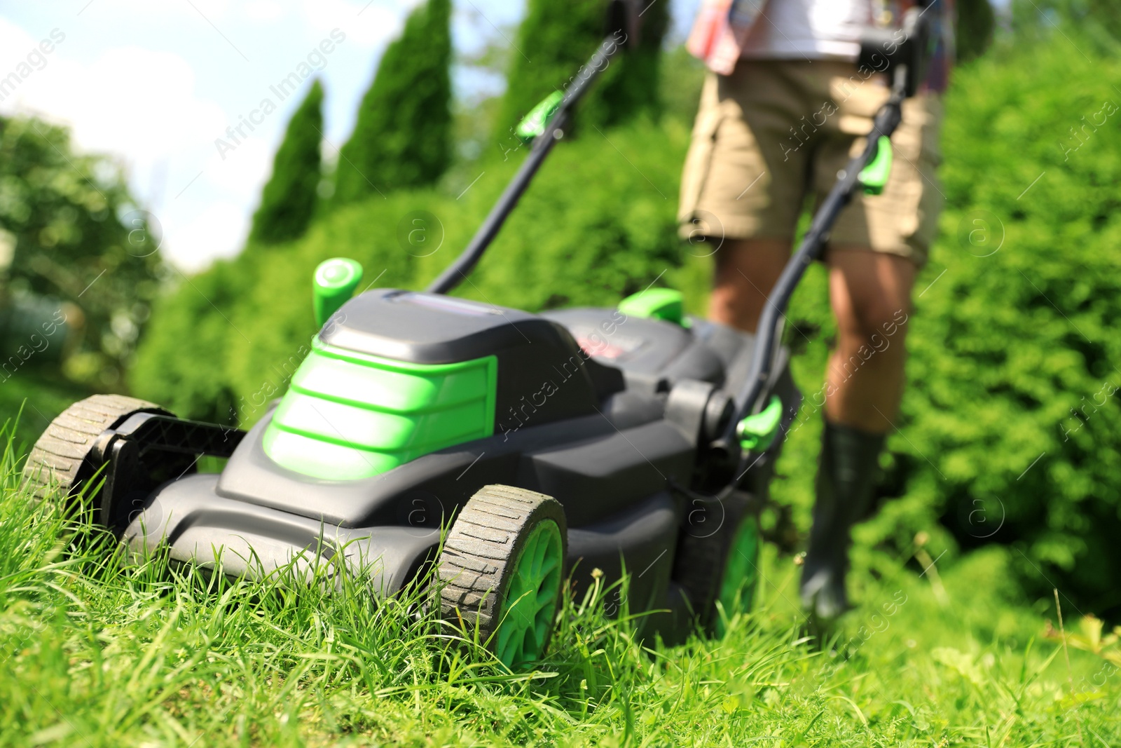 Photo of Man cutting grass with lawn mower in garden on sunny day, closeup