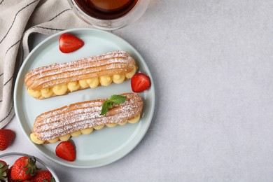 Photo of Delicious eclairs filled with cream, strawberries and mint on light table, top view. Space for text