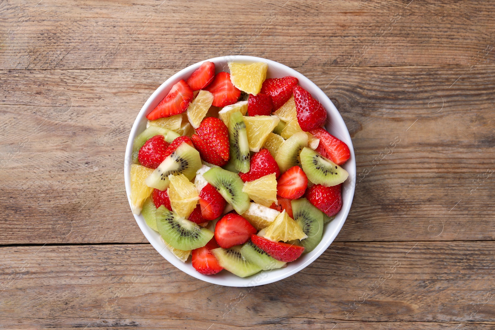 Photo of Delicious fresh fruit salad in bowl on wooden table, top view