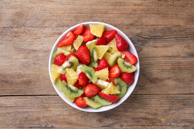 Photo of Delicious fresh fruit salad in bowl on wooden table, top view