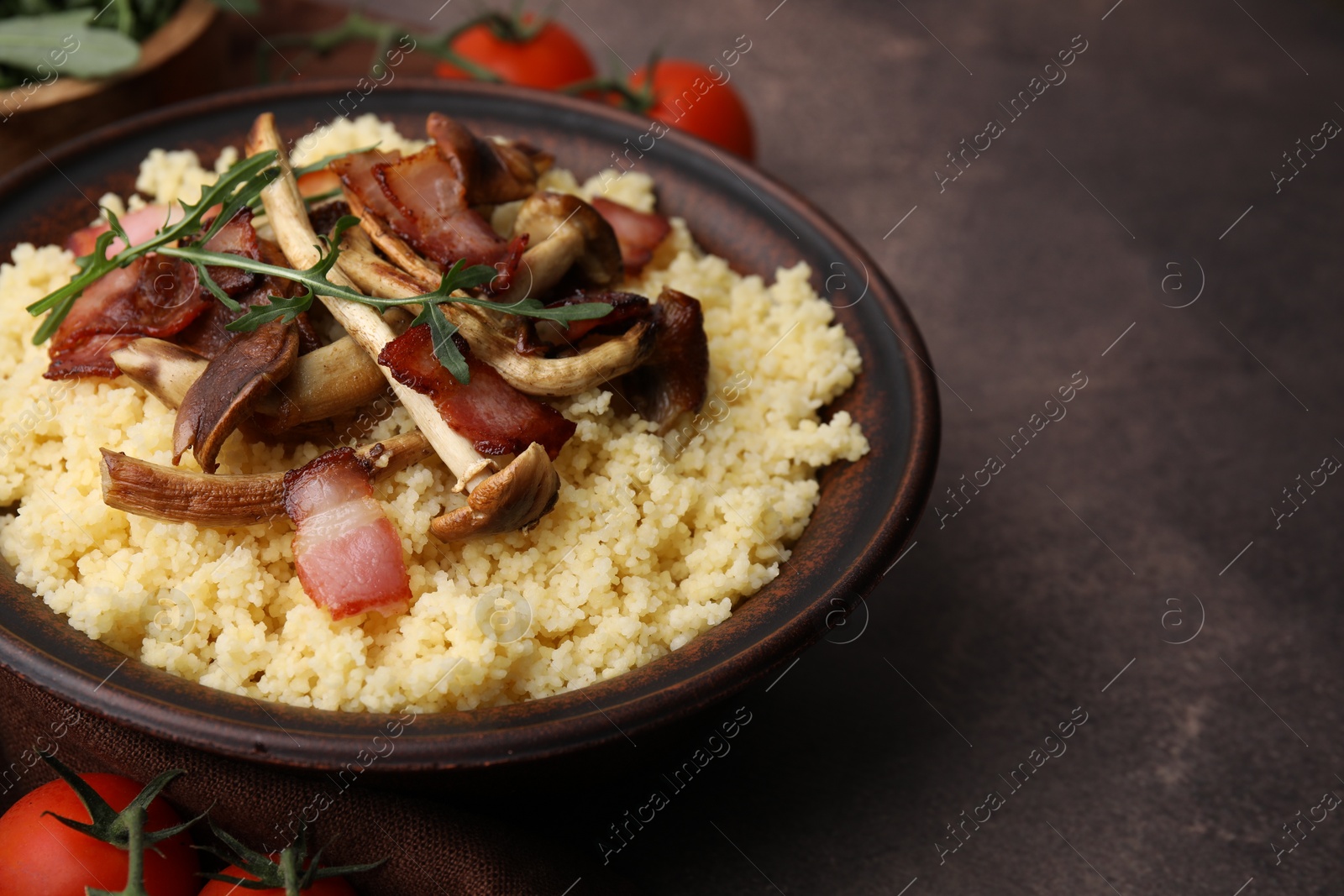 Photo of Tasty couscous with mushrooms and bacon in bowl on brown table, closeup. Space for text