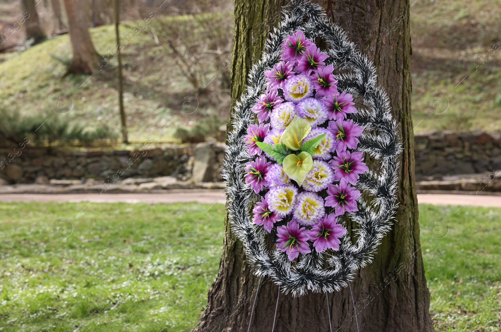 Photo of Funeral wreath of plastic flowers on tree outdoors