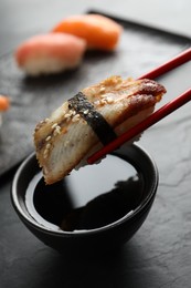 Photo of Dipping delicious nigiri sushi into soy sauce on black table, closeup