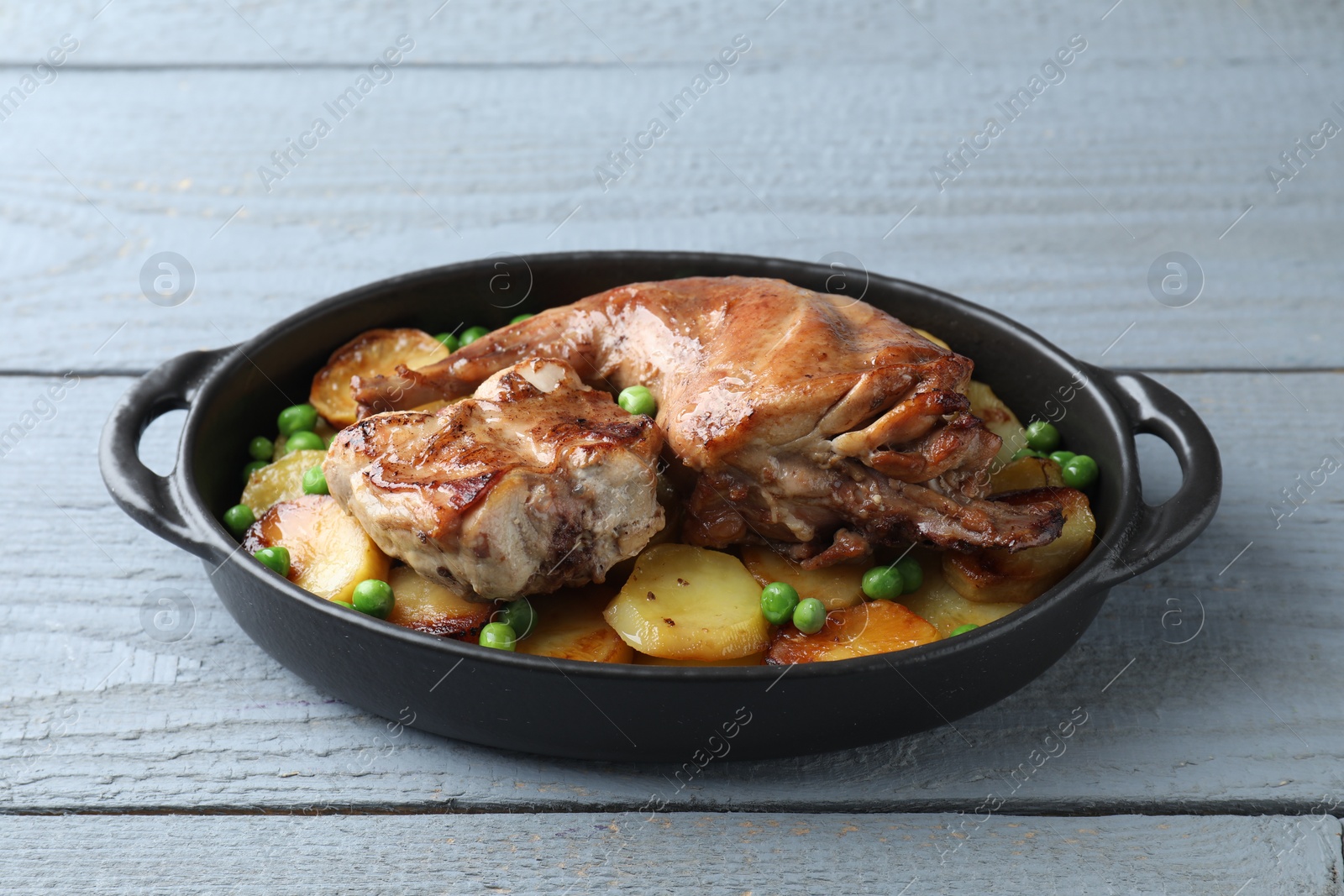 Photo of Tasty cooked rabbit with vegetables in baking dish on grey wooden table