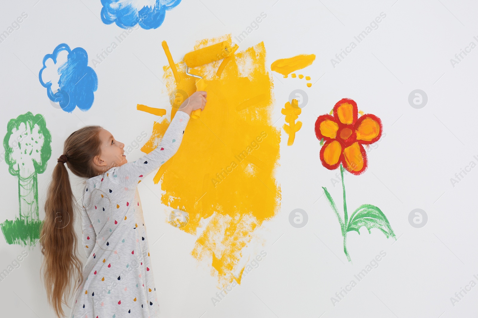 Photo of Little child painting wall with roller brush indoors