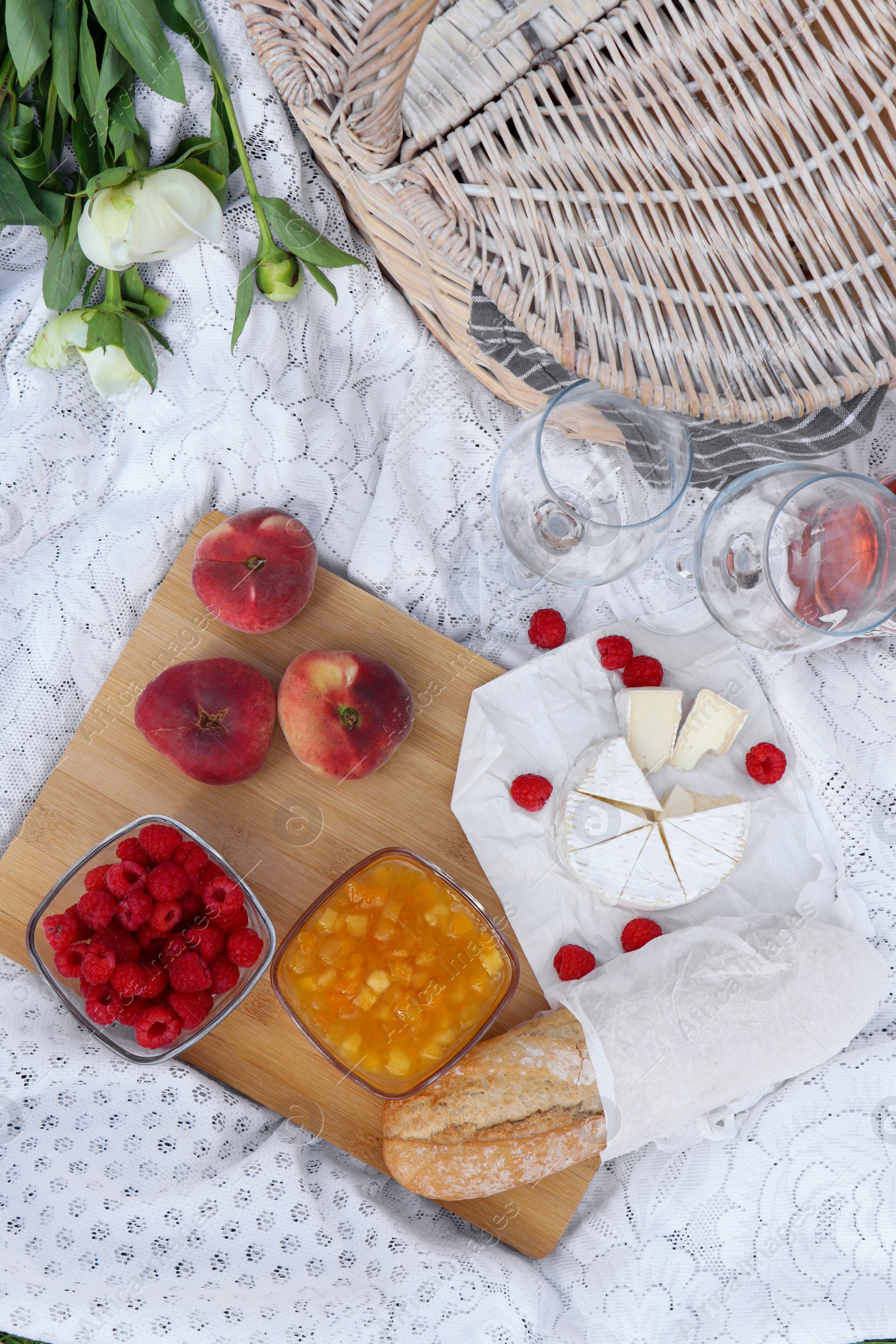 Photo of White picnic blanket with tasty food, flowers and basket, flat lay